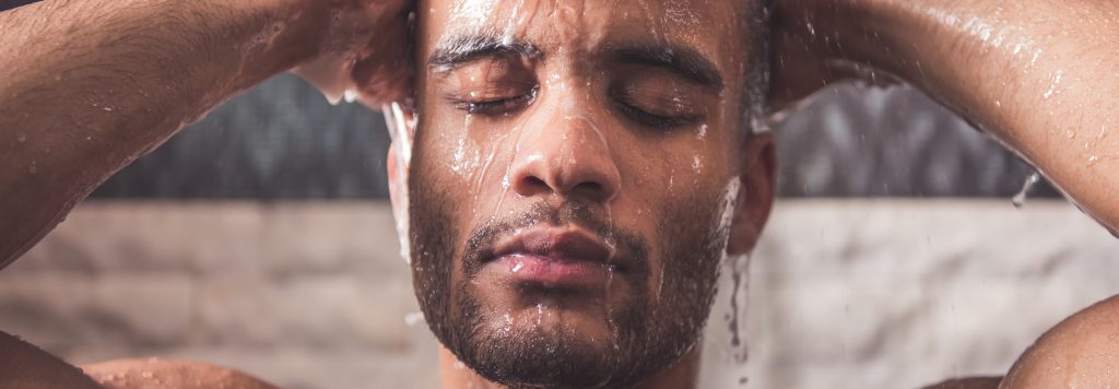 Handsome naked Afro American man is taking shower in bathroom